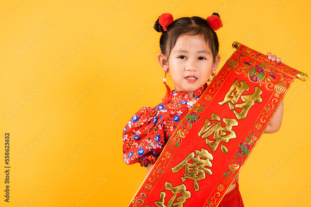 Chinese New Year. Happy Asian Chinese little child girl smile wearing red cheongsam qipao Spring festival couplets (Character FU means fortune, blessing), studio short isolated on yellow background Chinese New Year. Happy Asian Chinese little child girl smile wearing red cheongsam qipao Spring festival couplets (Character FU means fortune, blessing), studio short isolated on yellow background