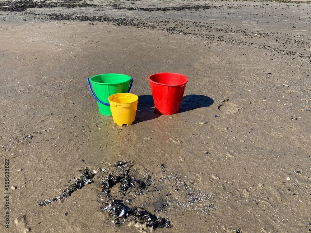Three colorful plastic buckets stand in the sand on the beach Three colorful plastic buckets stand in the sand on the beach