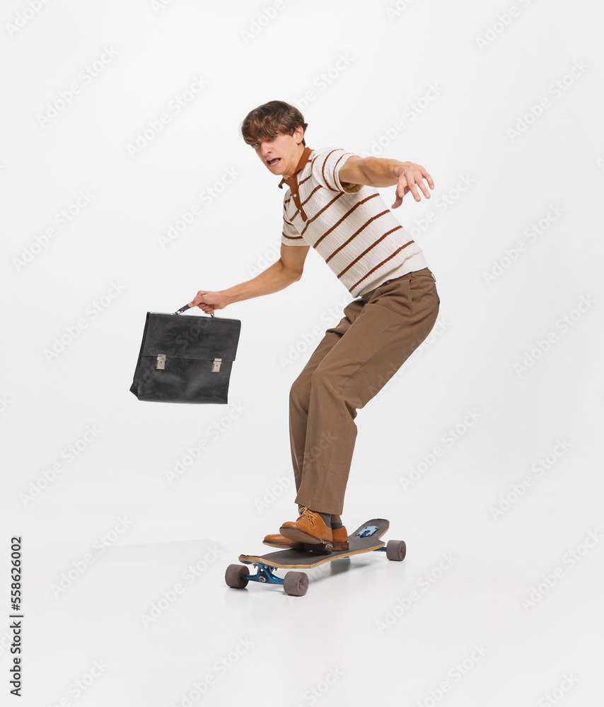 Young man, student in retro style clothes surfing on skateboard to studying isolated over white background. Young man, student in retro style clothes surfing on skateboard to studying isolated over white background.