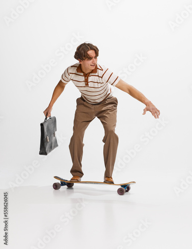 Photography Young man, student in retro style clothes surfing on skateboard to studying isolated over white background