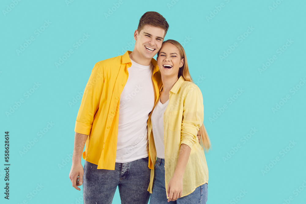 Naklejka premium Portrait of smiling young couple isolated on blue studio background hug and laugh enjoy healthy relationships. Happy man and woman embrace show love and care. Relations concept.