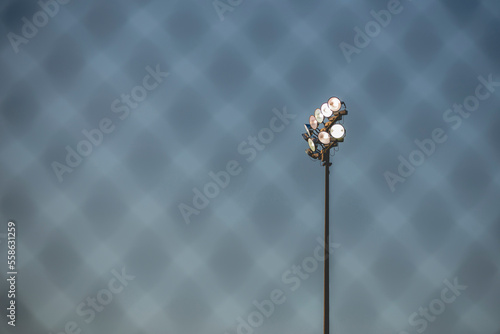 Low angle view of floodlight against sky seen through fence at baseball stadium photo
