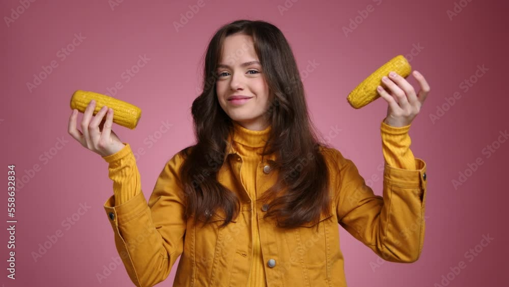 Portrait of happy teenager looking at camera with pink isolated background behind. Close-up shot of a smiling young woman holding corn. High quality 4k footage Portrait of happy teenager looking at camera with pink isolated background behind. Close-up shot of a smiling young woman holding corn. High quality 4k footage