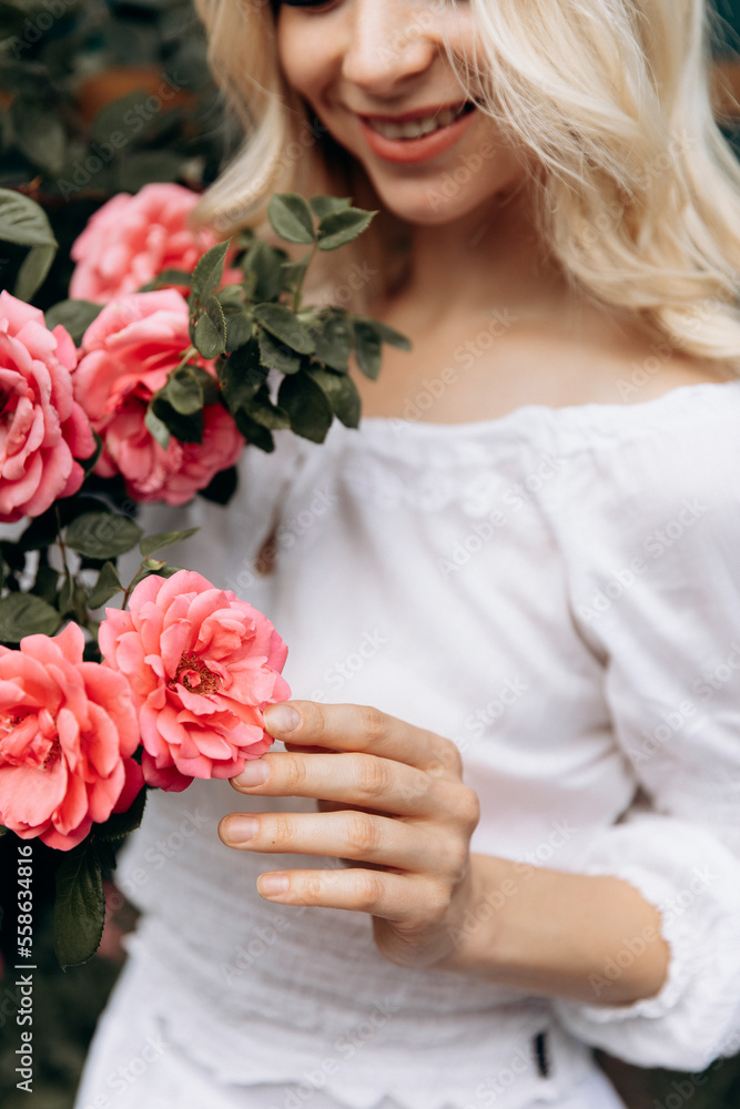 Naklejka premium attractive model among floral roses in a white dressattractive model among floral roses in a white dress. focus on the hands
