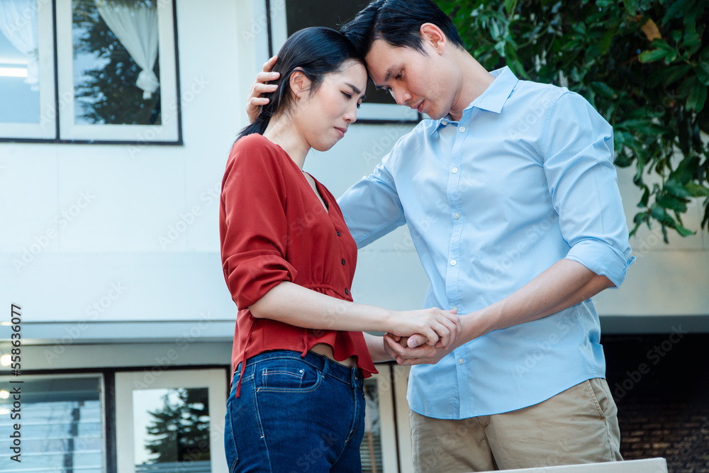 Fototapeta premium Man comforting his wife and woman hugging her husband and cry in front of the house and full of cardboard boxes during the transport in move out day, moving home concept