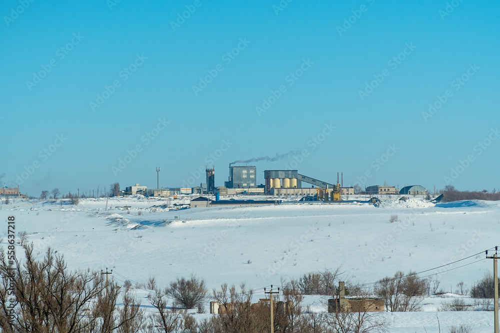 A small factory with a pipe on a snow-covered field against a blue sky background