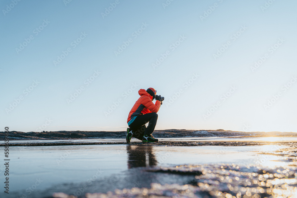 man photographing the sunset crouched down