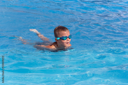 Boy child in swimming goggles with float board tool swim in pool. Summer holiday, family vacation, water sport