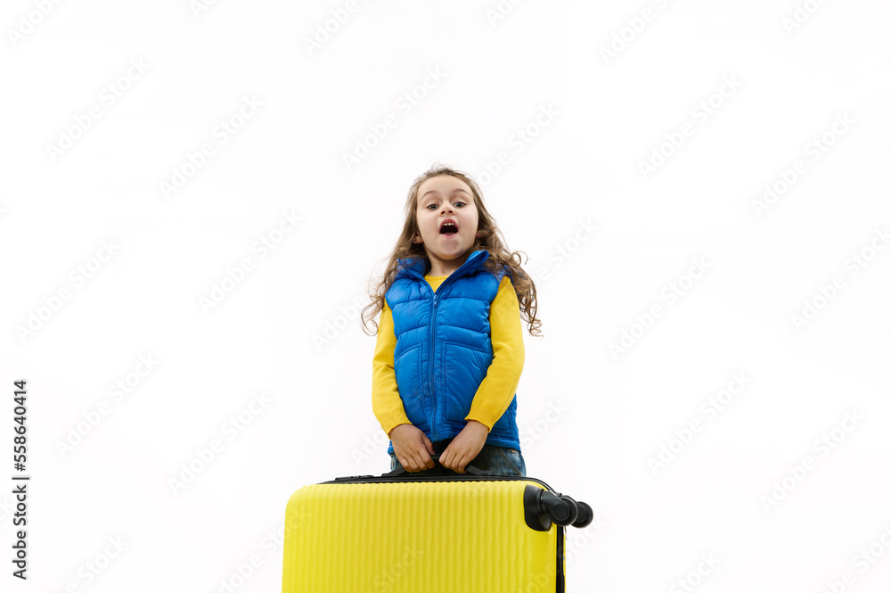 Caucasian beautiful little kid girl in blue jacket, going for weekend getaway, carrying a heavy yellow suitcase, isolated on white background. Travel. Trip. Journey. Air Flight. Copy advertising space Caucasian beautiful little kid girl in blue jacket, going for weekend getaway, carrying a heavy yellow suitcase, isolated on white background. Travel. Trip. Journey. Air Flight. Copy advertising space