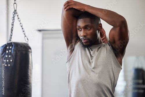 Black man stretching, boxing gym and training for fitness, wellness or focus for strong body. Man, punching bag and warm up muscle with vision, goal or development in workout, mma exercise or health photo