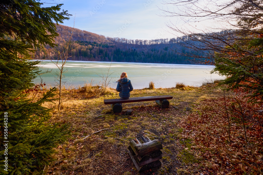 a woman sitting and looking towards a lake