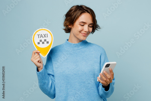 Murais de parede Young smiling happy cheerful caucasian woman wear knitted sweater use mobile cell phone booking taxi cab isolated on plain pastel light blue cyan background studio portrait