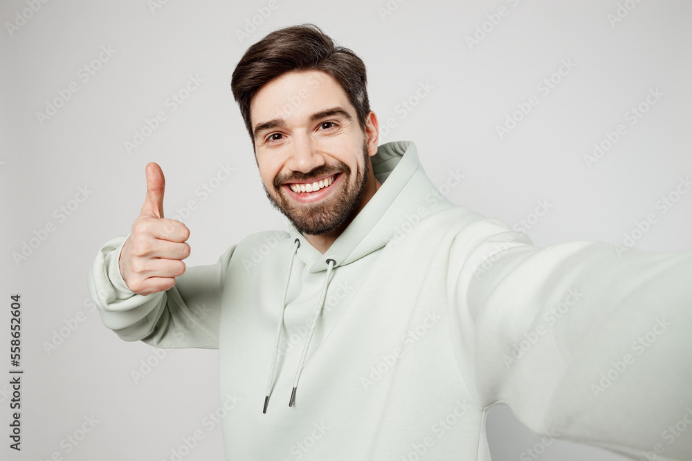Close up young fun caucasian man wear mint hoody look camera doing selfie shot pov on mobile cell phone show thumb up isolated on plain solid white background studio portrait People lifestyle concept Close up young fun caucasian man wear mint hoody look camera doing selfie shot pov on mobile cell phone show thumb up isolated on plain solid white background studio portrait People lifestyle concept