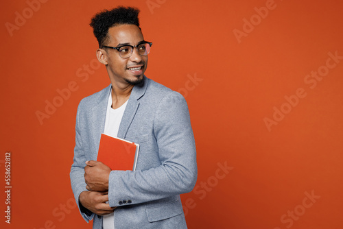 Young happy fun employee business man corporate lawyer wear classic formal grey suit shirt glasses work in office hold in ahnds diary look aside on area isolated on plain red orange background studio. photo