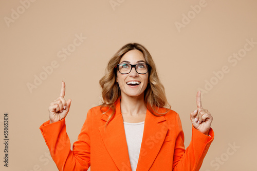 Young employee business woman corporate lawyer 30s in classic formal orange suit glasses work in office point index finger overhead on worspace area mock up isolated on plain beige background studio