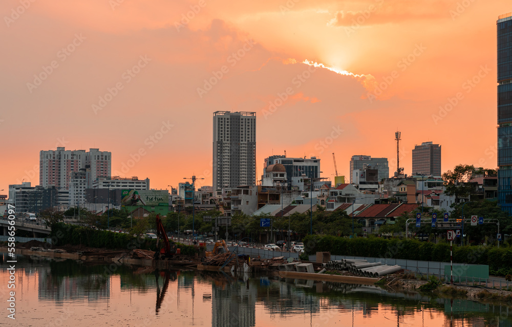 HOCHIMINH CITY, VIETNAM - JANUARY 19, 2022: beautiful sunset sky with rare orange-pink color, the sun is round like egg yolk, foreground is Saigon river and old houses