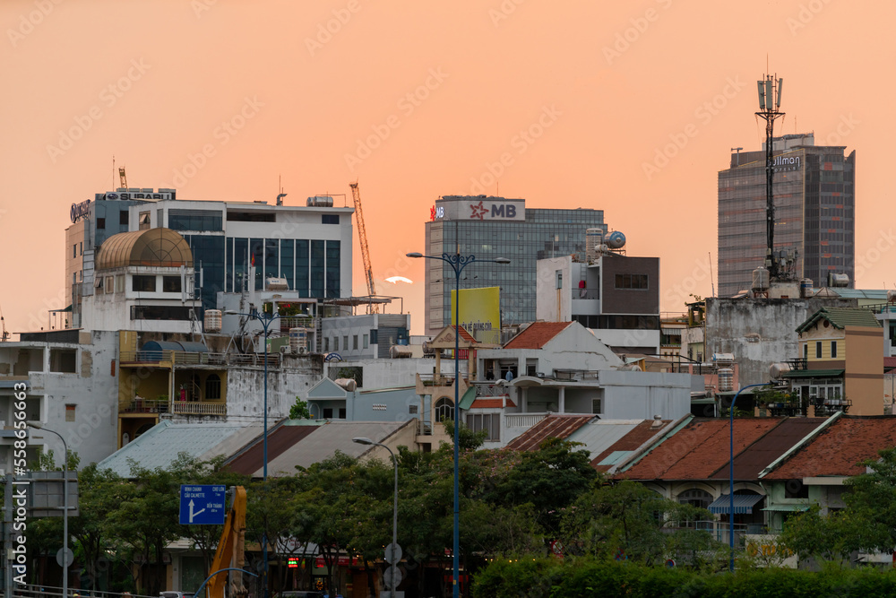 HOCHIMINH CITY, VIETNAM - JANUARY 19, 2022: beautiful sunset sky with rare orange-pink color, the sun is round like egg yolk, foreground is Saigon river and old houses