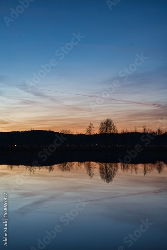 Wonderful blue golden red sky after sunset with trees in foreground at a lake with its reflections 