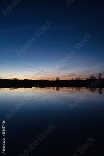 Wonderful blue golden red sky after sunset with trees in foreground at a lake with its reflections 