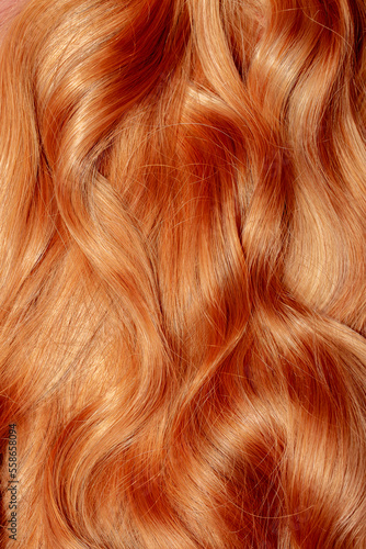 Red hair close-up as a background. Women s long orange hair. Beautifully styled wavy shiny curls. Hair coloring bright shades. Hairdressing procedures  extension.