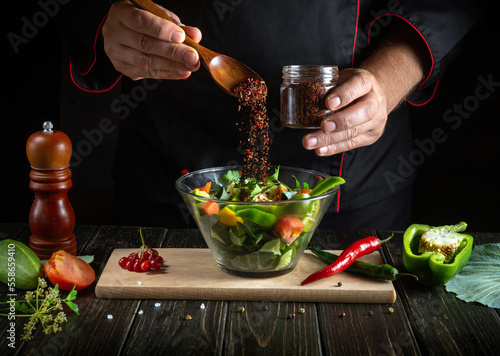 Professional chef adds aromatic seasoning to vegetarian food. Cooking delicious salad by the hands of the cook in the kitchen. Menu idea for a hotel or restaurant