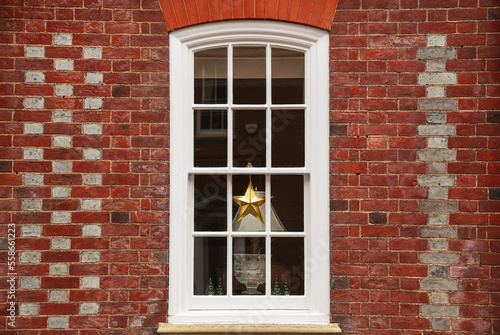 Beautiful Christmas decoration placed in front of a white wooden window on a brick facade building. British English architecture house design.
