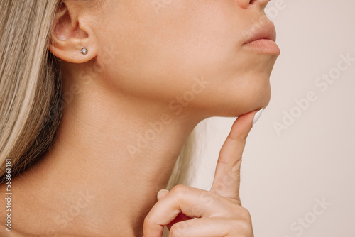 Close up of young caucasian blonde woman pointing at her chin with her finger. Dimple on the chin isolated on a beige background. Mentoplasty concept