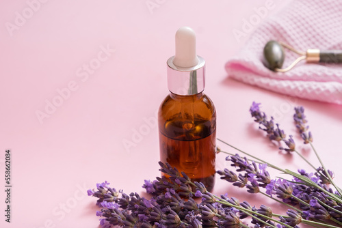 Dropper bottle and face skin massager with lavender flowers on colored background