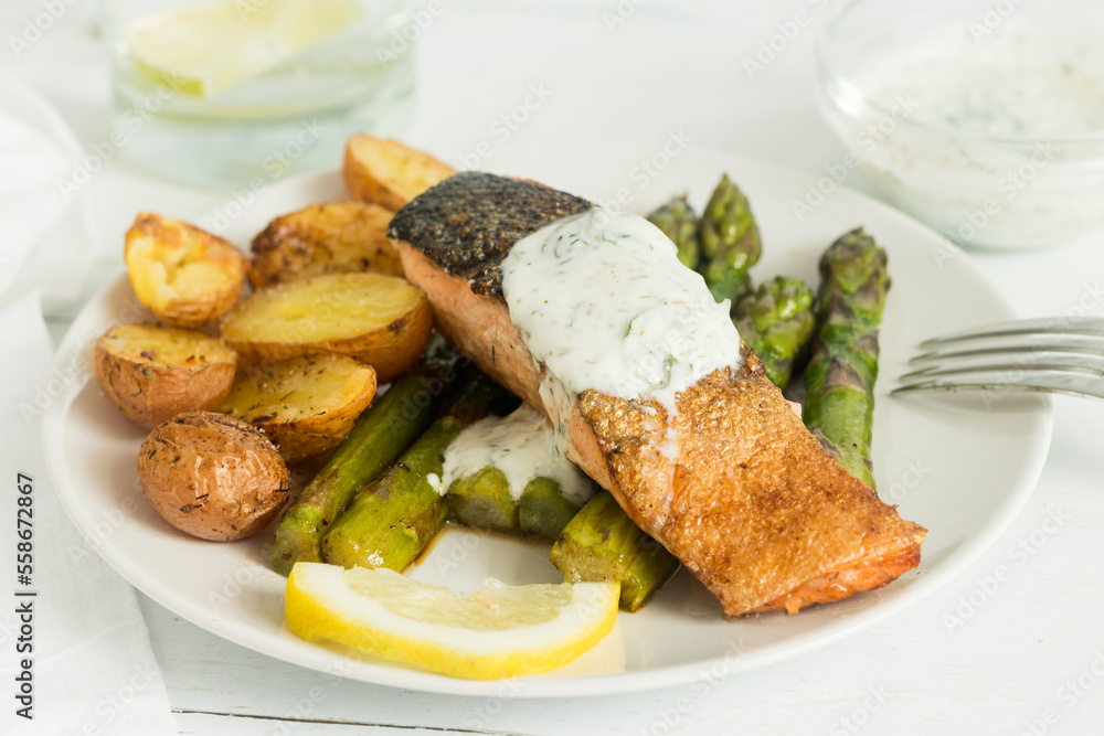 One plate of roasted salmon with steak potatoes, asparagus, yogurt sauce and lemon. One plate of roasted salmon with steak potatoes, asparagus, yogurt sauce and lemon.