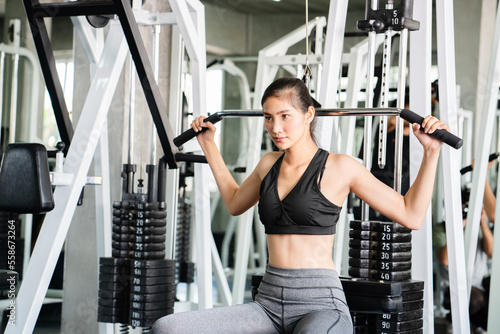 Asian woman doing weight training by weight machine Down Bar play on shoulder and upper arms to be strong and toned in gym. Bodyweight helps to burn excess fat. and build muscle. exercise for health photo