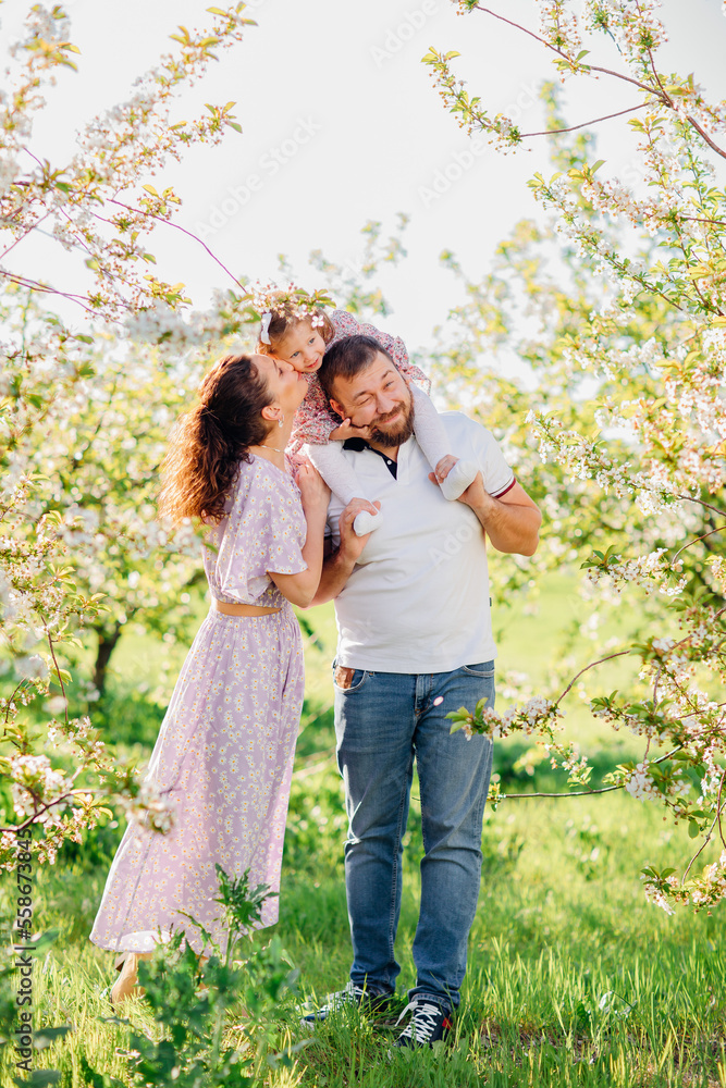 a mom and a dad with a baby daughter in a blooming spring garden. happy family. 