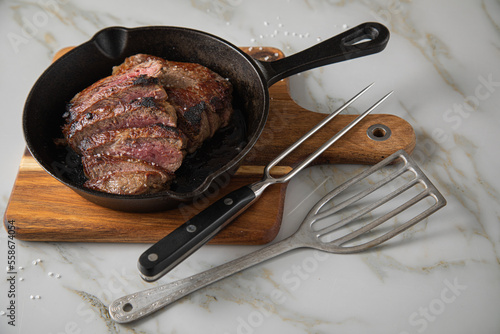 Entrecote Steak vom Rind medium rare gebraten in Gusseisen Pfanne mit Meersalz auf Holzbrett mit Messer, Fleischgabel und hellen Marmor Hintergrund photo