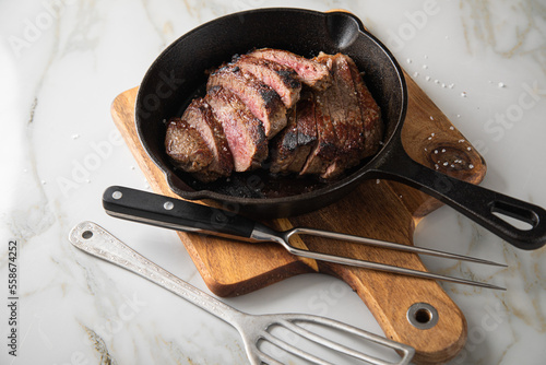 Entrecote Steak vom Rind medium rare gebraten in Gusseisen Pfanne mit Meersalz auf Holzbrett mit Messer, Fleischgabel und hellen Marmor Hintergrund photo