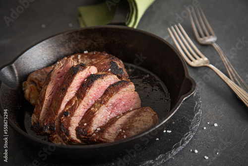 Entrecote Steak vom Rind medium rare gebraten in Gusseisen Pfanne mit Meersalz auf schwarzen Schiefer mit Gabel, grünen Tuch und dunklen Stein Hintergrund photo