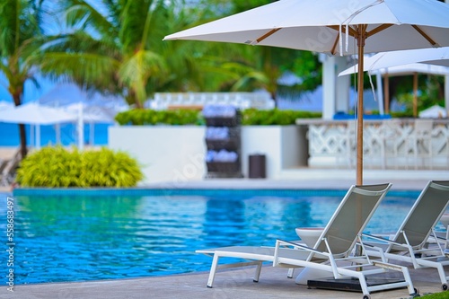 White sand beach and blue sea landscape view of a tropical resort hotel beside modern swimming pool, white parasols, palm trees, deck beach chairs in the golden sunset time