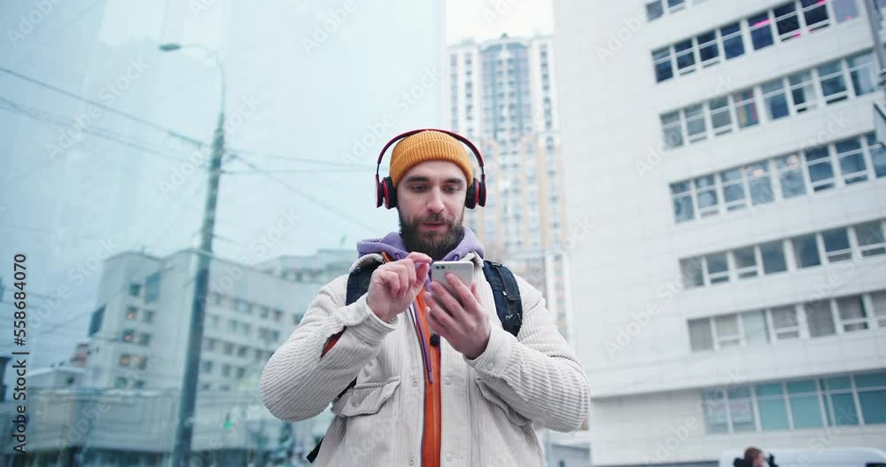 Handsome arab hipster man with beard wearing yellow hat using smartphone to listen to the music outdoors in the city streets at winter Handsome arab hipster man with beard wearing yellow hat using smartphone to listen to the music outdoors in the city streets at winter