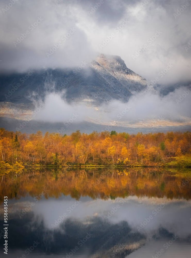 Autumn forest is reflected in the water of lake in the misty mountains Autumn forest is reflected in the water of lake in the misty mountains