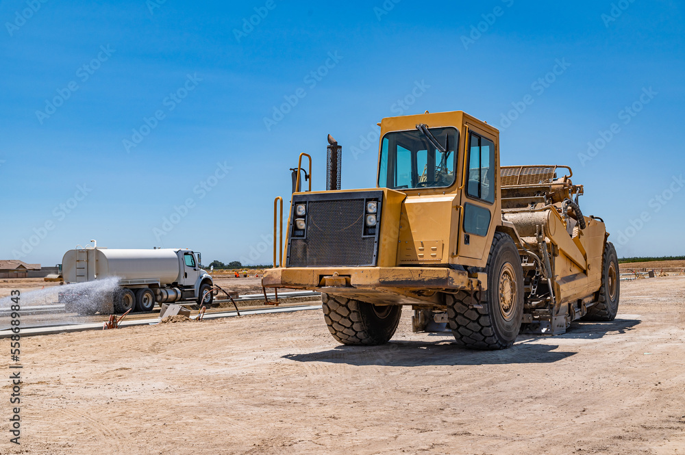 Yellow tractor, road repair. Side view. Watering machine in the background.