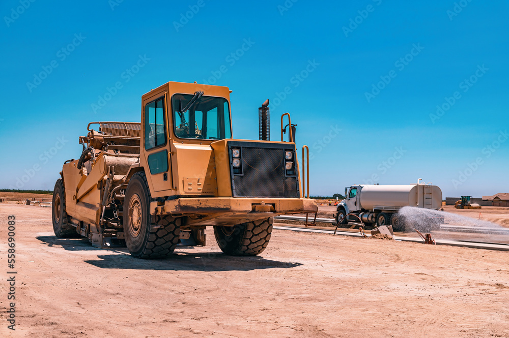 Side view of a large yellow tractor. The watering machine waters the road. Construction of the highway. Side view of a large yellow tractor. The watering machine waters the road. Construction of the highway.