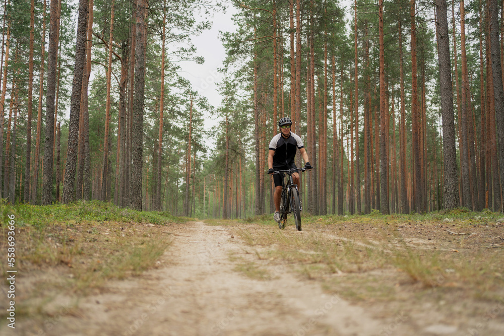 A male cyclist in the woods riding a bicycle with a helmet, using a GPS activity tracker watch while training on a bicycle.