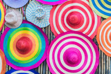 A variety of fashionable and colorful hats hanging on the bamboo backdrop of curbside shop. Women's designer hats from the sun of different colors. Design of women's beach hats. Beach hats for summer.