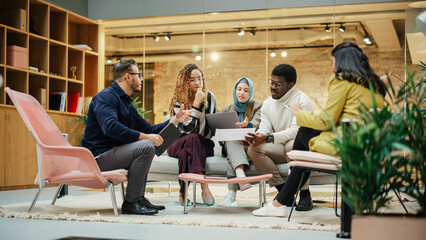 Multiethnic Group of Creative People Working on Project in a Modern Bright Office. A Diverse Group of Colleagues Developing a New Approach Using Charts, Laptop, and Tablet. Wide Shot