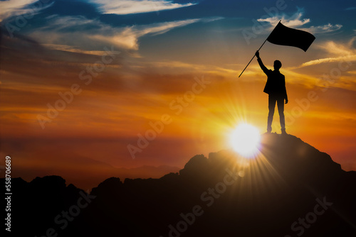 Silhouette of a businessman holding a flag on the top of the mountain. Sunrise background. Business, success, and leadership concepts. Image Illustration.