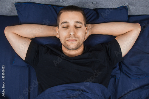 Top view of a handsome young man sleeping comfortably on the bed in his bedroom at night. Bachelor bedroom. Deep sleep. © Yuliia