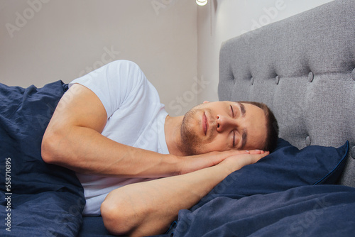 Top view of a handsome young man sleeping comfortably on the bed at night in his bedroom. Sleep in different positions. Bachelor bedroom. Deep sleep.