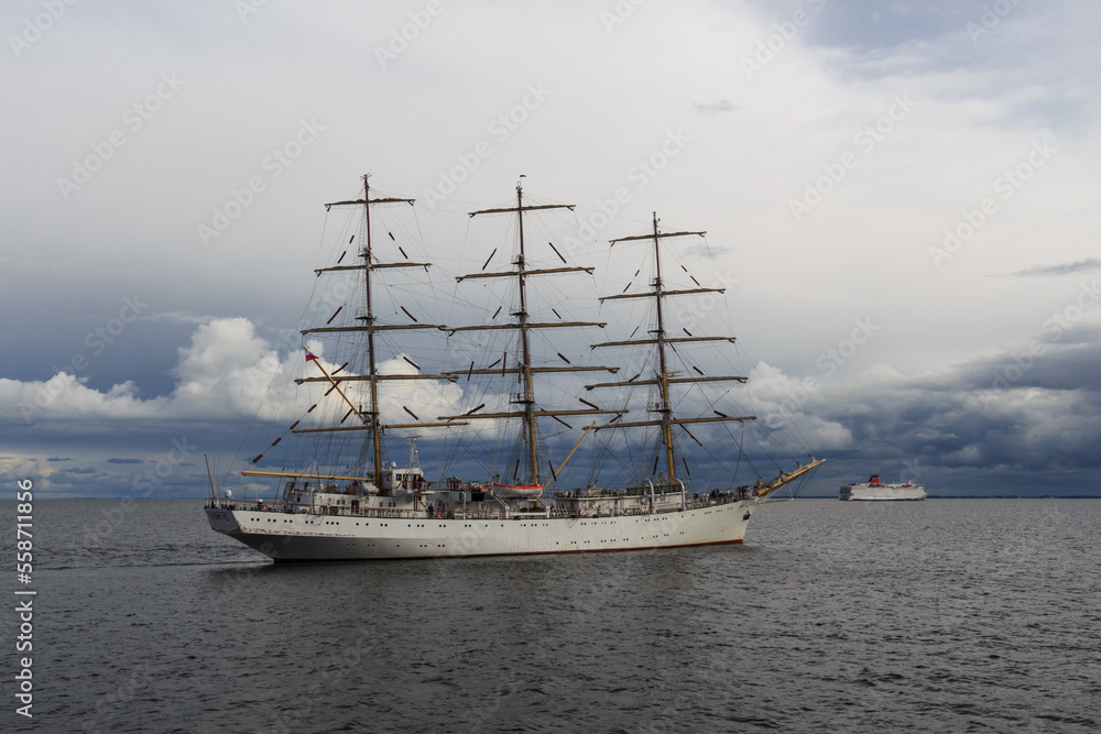 Three-masted sailing frigate goes to sea from the port against a stormy sky.