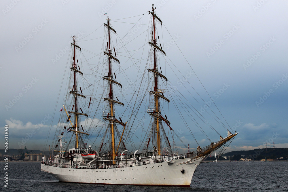 Three-masted sailing frigate goes to sea from the port against a stormy sky. Three-masted sailing frigate goes to sea from the port against a stormy sky.