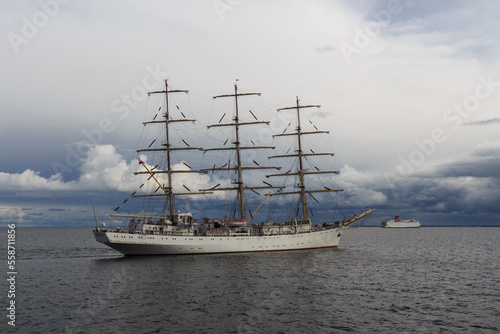 Three-masted sailing frigate goes to sea from the port against a stormy sky.