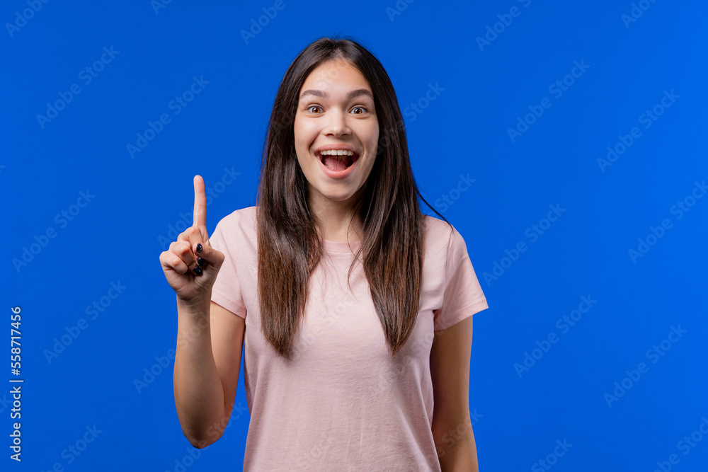 Happy teen girl having idea eureka moment, pointing finger up on blue background. Smart student woman showing answer gesture or remembered what she forgot, memory concept Happy teen girl having idea eureka moment, pointing finger up on blue background. Smart student woman showing answer gesture or remembered what she forgot, memory concept