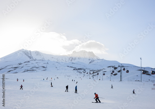 Erciyes, Kayseri, Turkey - 02.23.2022: Skiers go downhill skiing on snow-covered mountain ski slope against the backdrop of a cloudy sky and ski lifts. Winter. Extreme sport and travel content